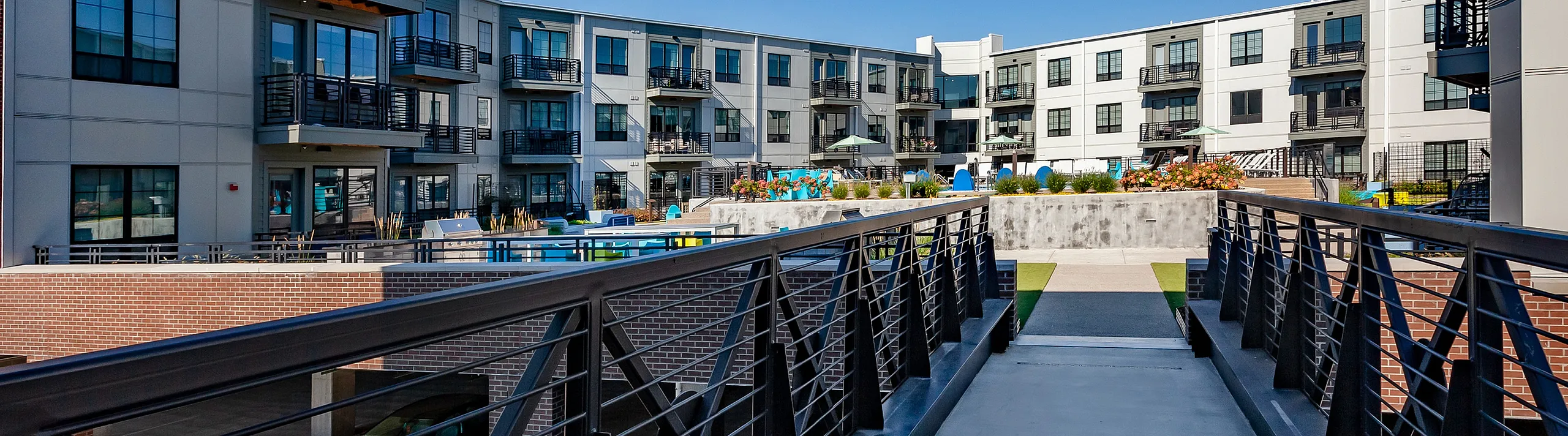 Modern apartment complex with balconies and a sleek pedestrian bridge under a clear blue sky.