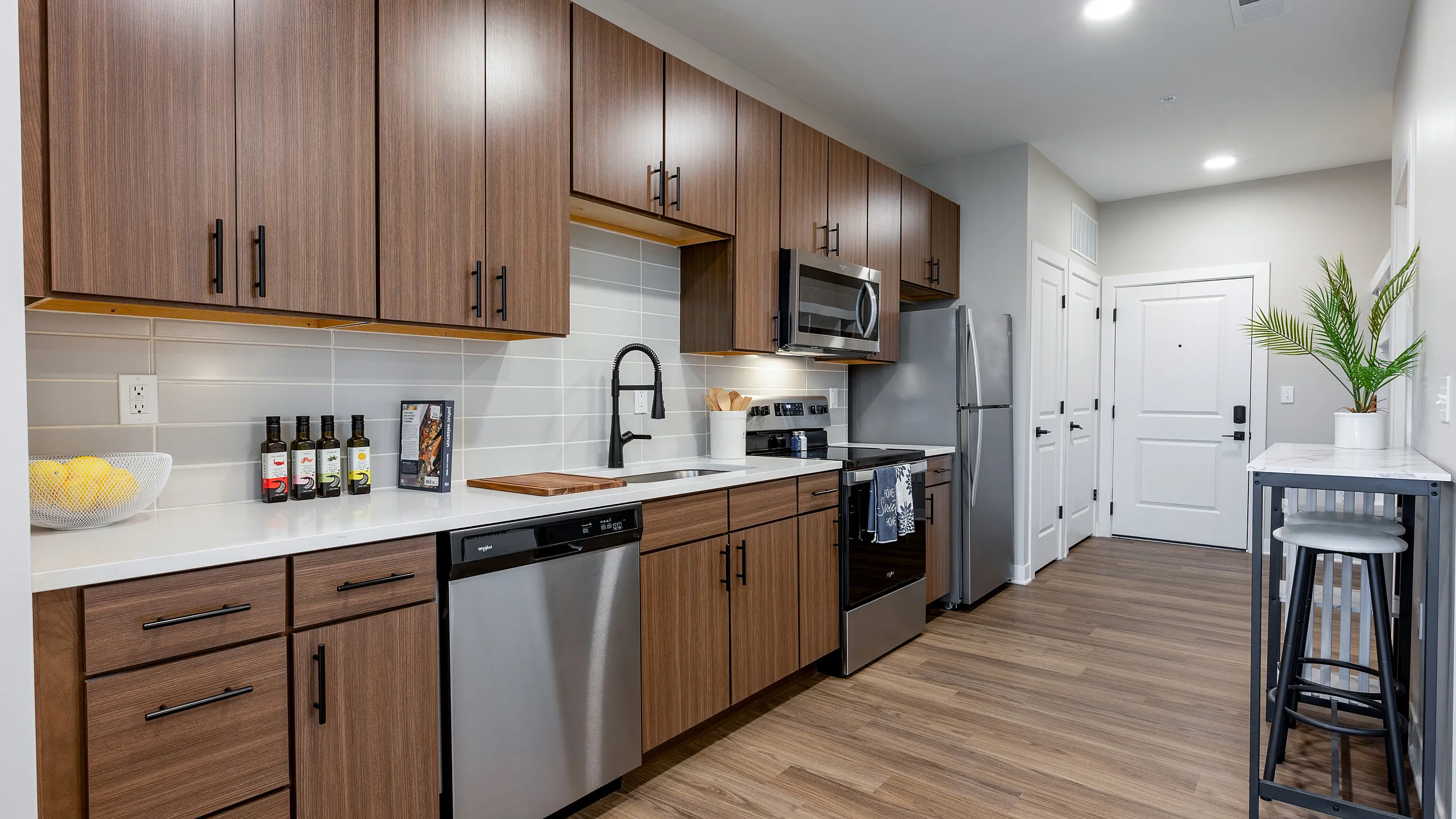 Modern kitchen with sleek wood cabinetry, stainless steel appliances, and elegant countertop; features bar stool seating and tasteful decor.