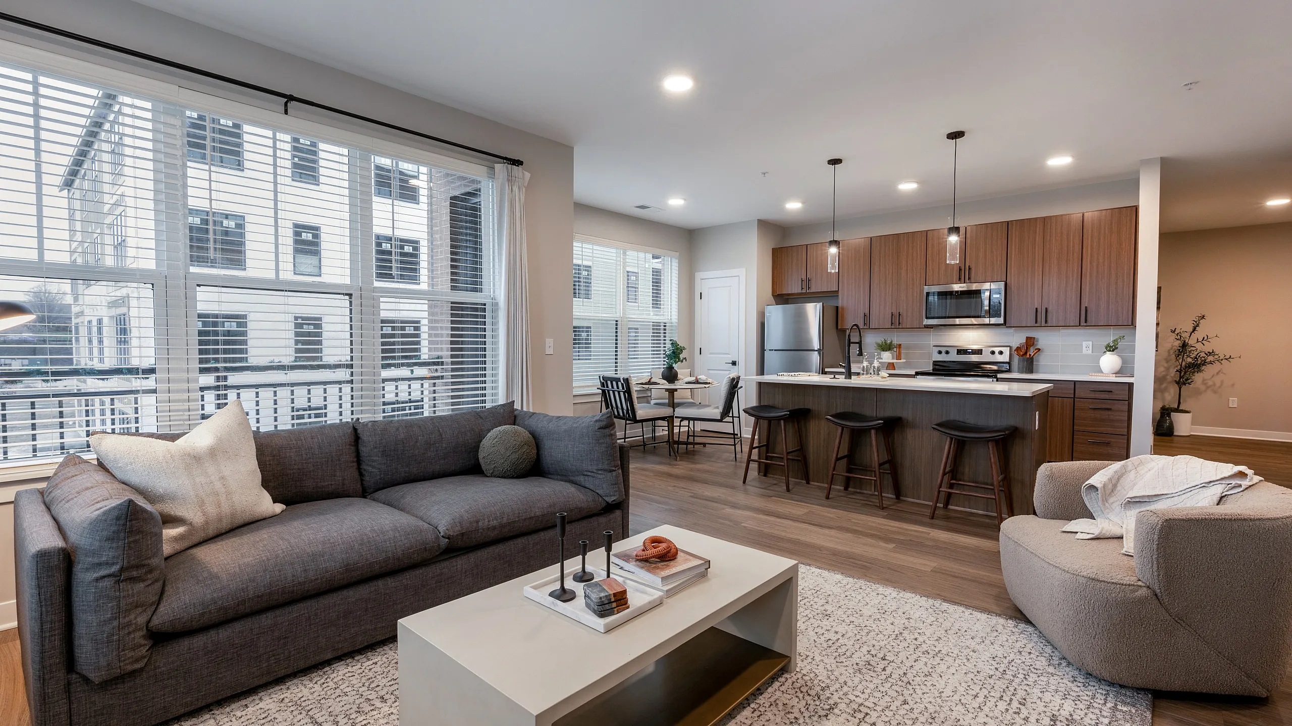Modern open-plan living area featuring a cozy gray sofa, stylish kitchen with stainless steel appliances, and large windows inviting natural light.