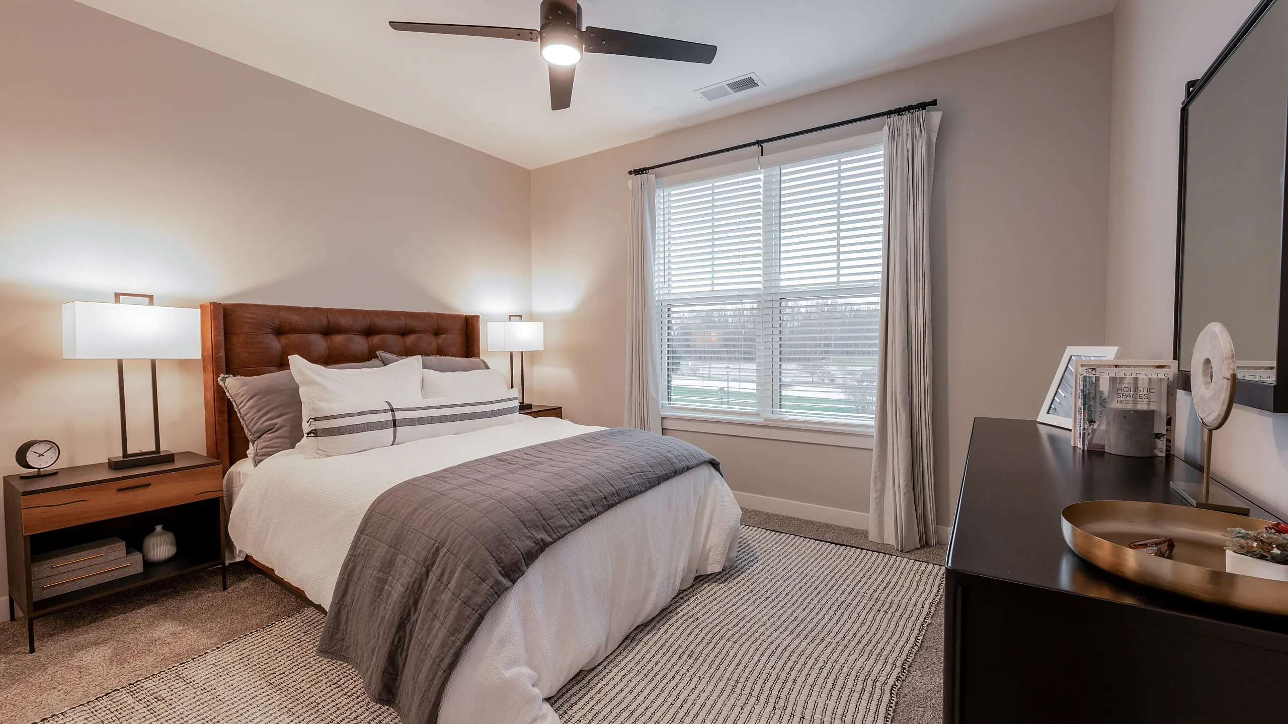 Elegant bedroom featuring a plush bed with a tufted headboard, modern bedside lamps, and large window with a serene view.