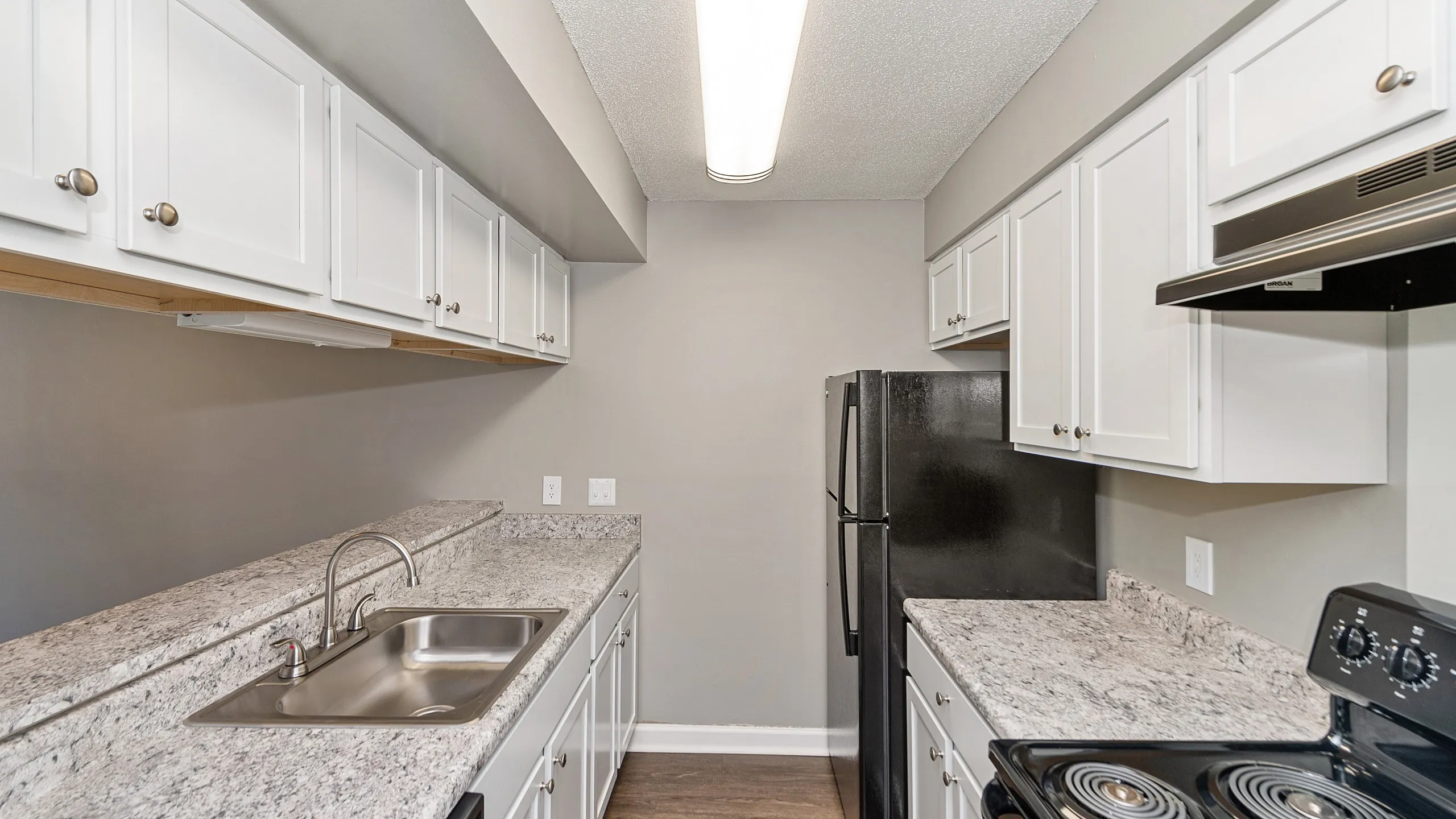 Modern kitchen with sleek granite countertops, white cabinetry, and stylish black appliances.