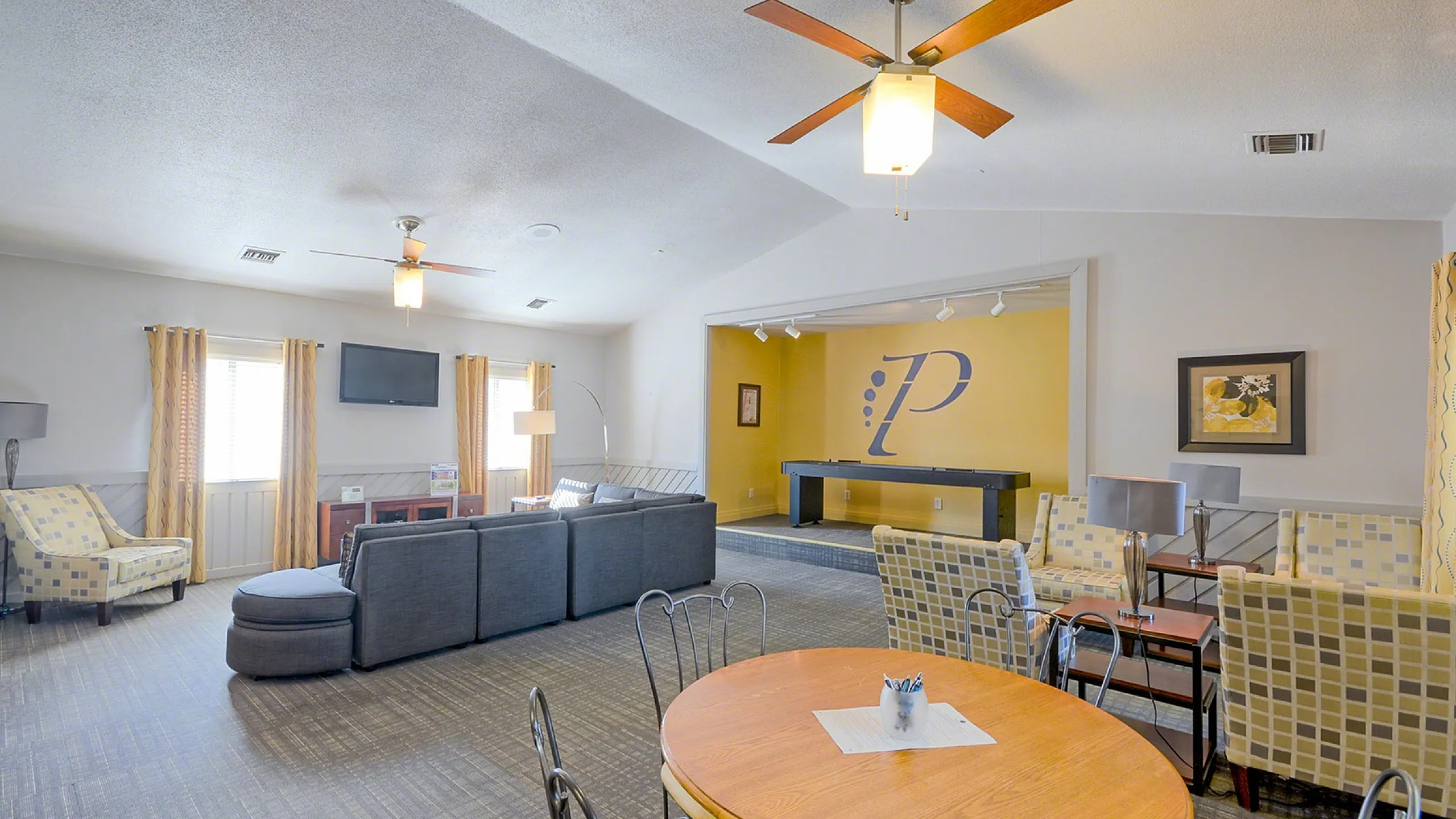 Spacious living area featuring modern furniture, ceiling fans, and a cozy entertainment space with large windows for natural light.