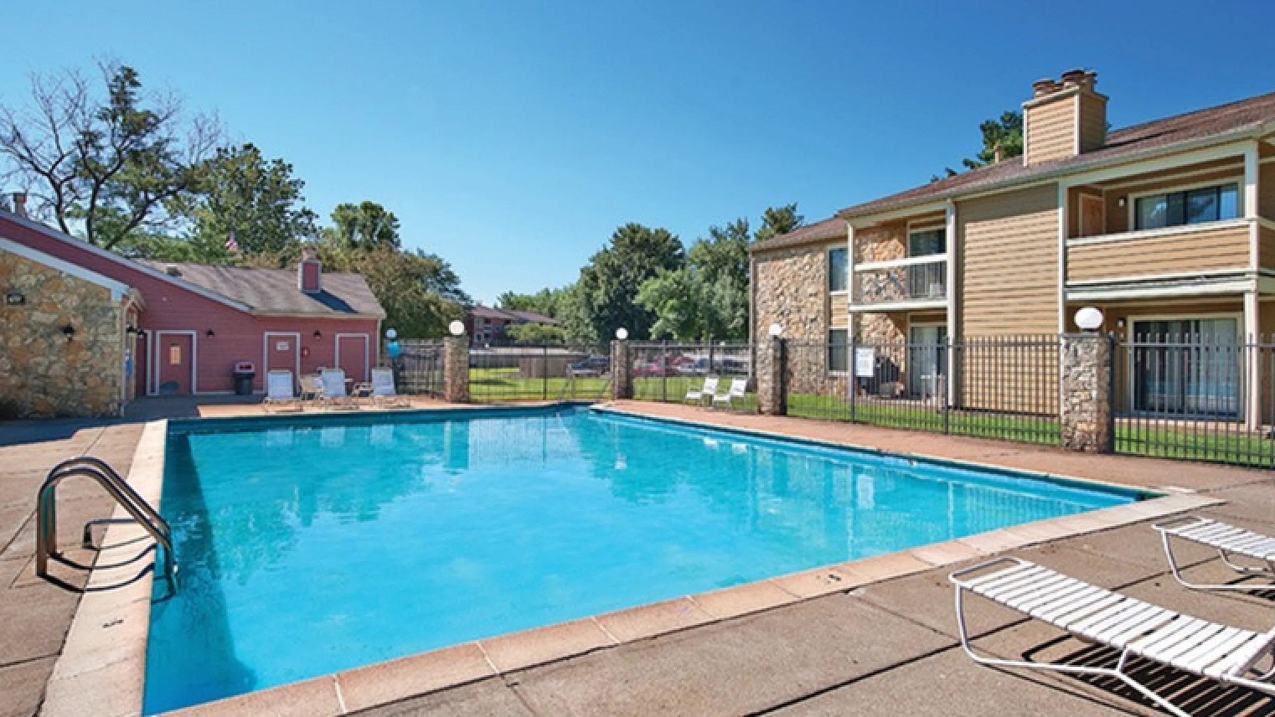 Inviting outdoor pool area with sun loungers, surrounded by stylish apartment buildings and lush greenery, perfect for relaxation and leisure.