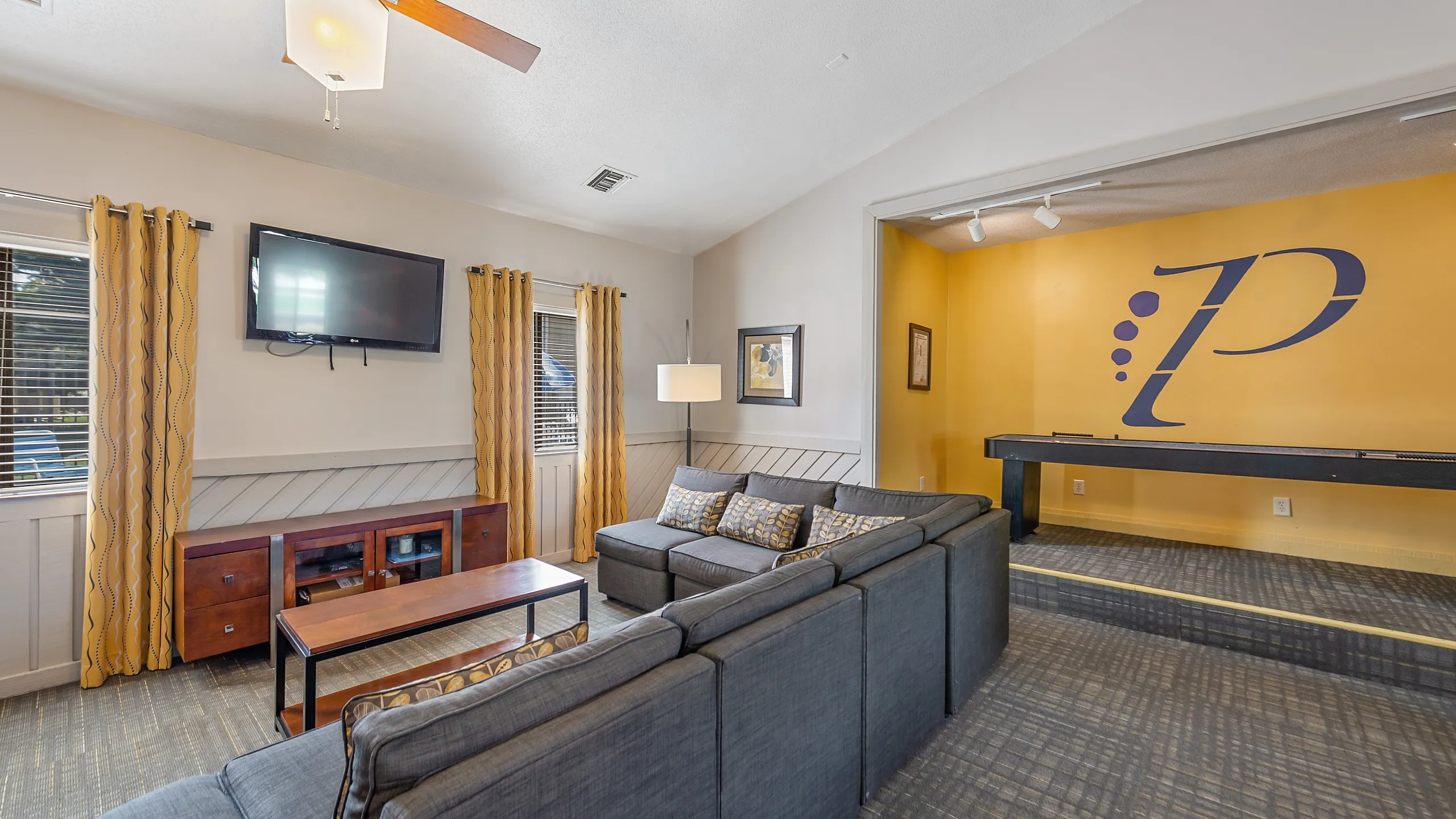 Contemporary living room with cozy gray sectional, vibrant yellow accents, and wall-mounted TV, offering a welcoming entertainment space.