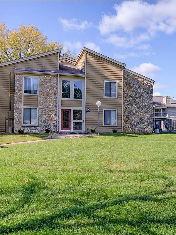 Charming apartment complex with rustic stone accents and lush green lawn under a bright blue sky.