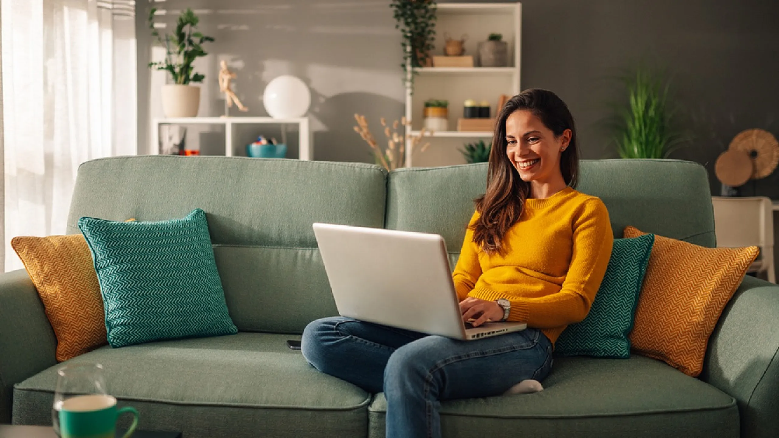 Bright and cozy living room with stylish decor, featuring a teal sofa adorned with vibrant cushions and a cheerful atmosphere.