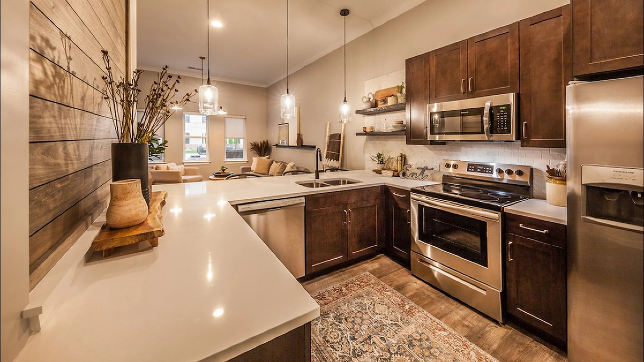 Modern kitchen with sleek dark cabinetry, stainless steel appliances, and elegant pendant lighting, seamlessly connecting to a cozy living area with warm wooden accents.