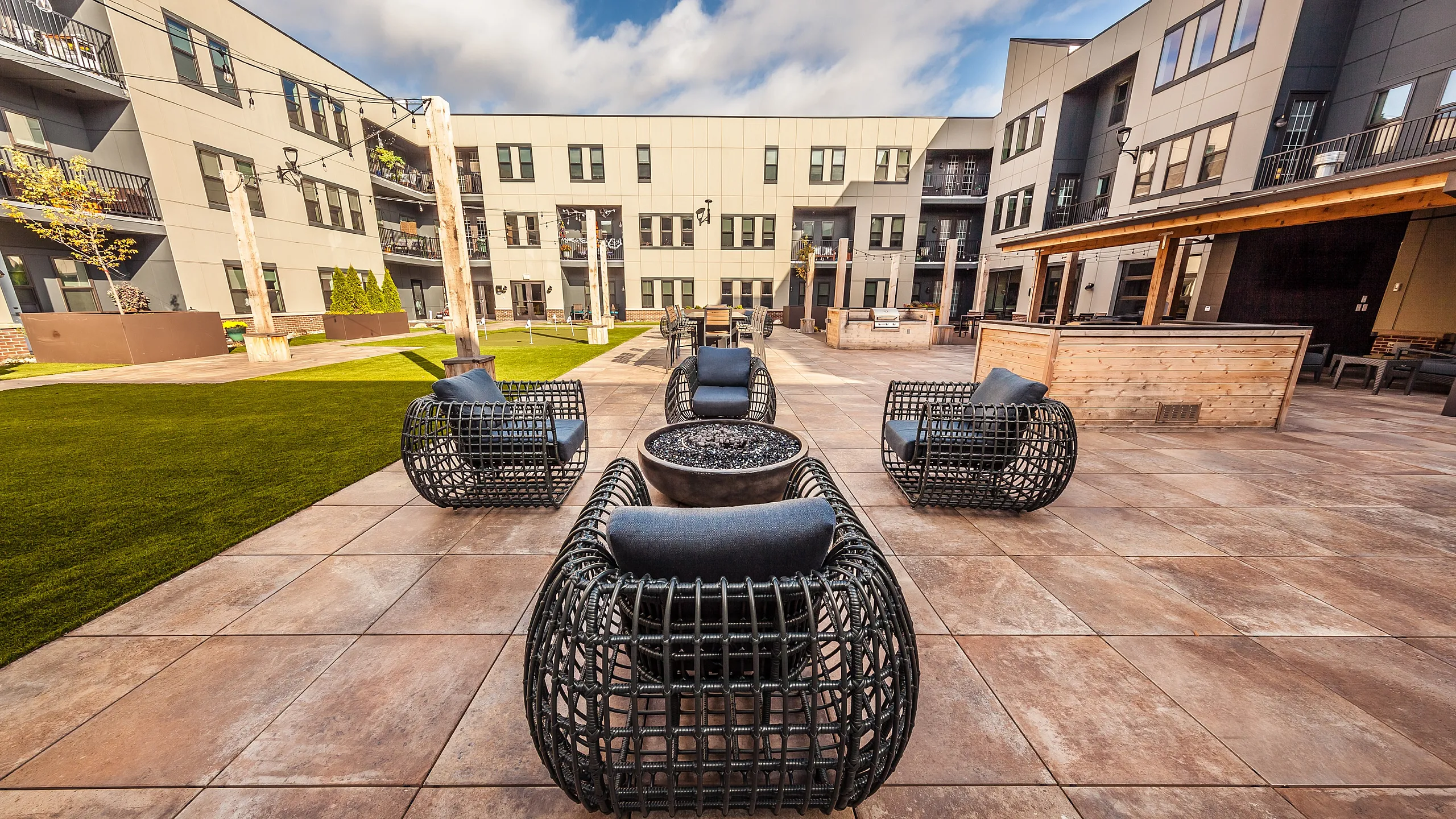 Chic outdoor courtyard featuring stylish modern seating, lush green lawns, and a contemporary architectural backdrop, perfect for social gatherings or relaxation.