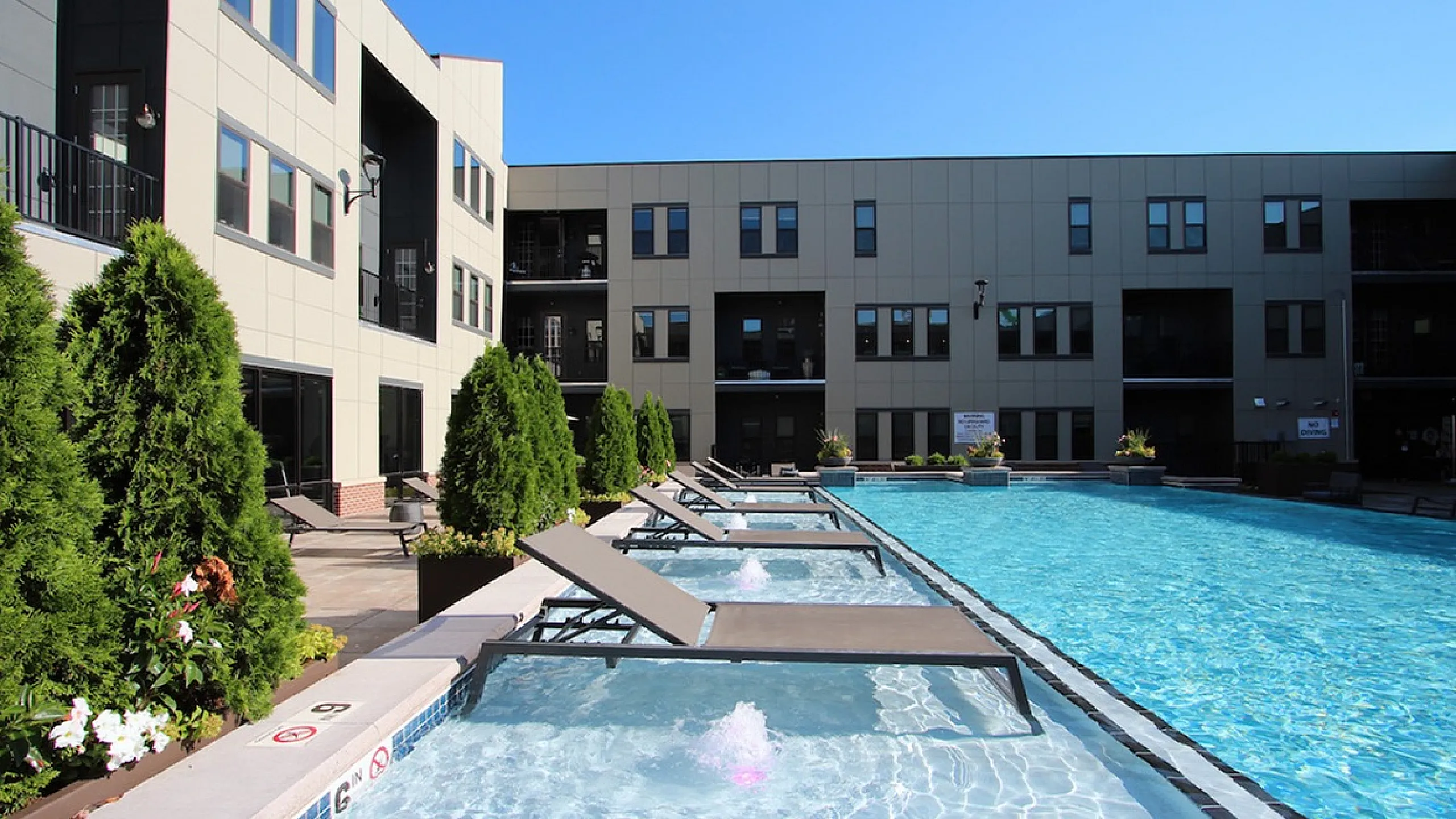 Luxurious apartment complex featuring an inviting pool with sun loungers, surrounded by lush greenery and modern architecture.
