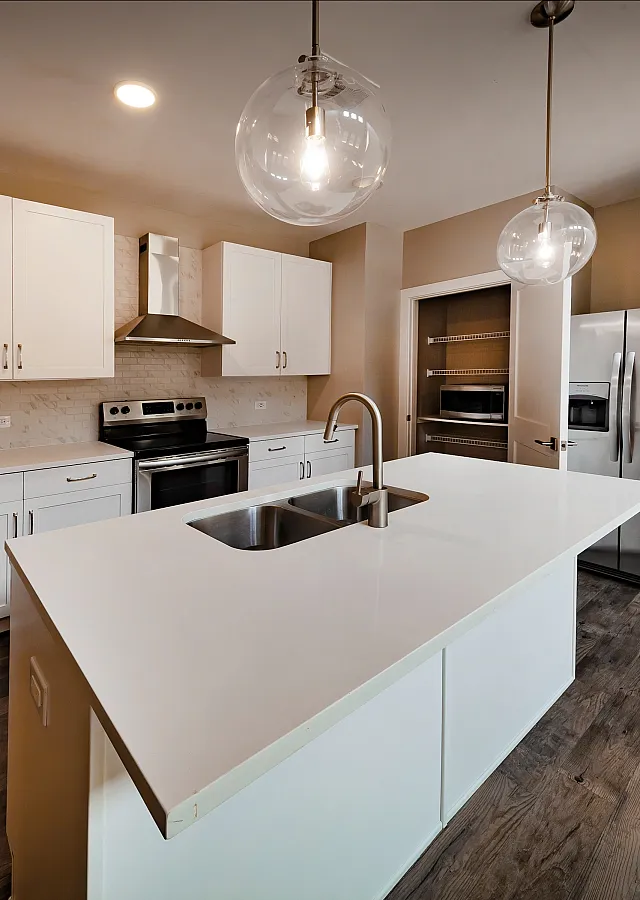 Modern kitchen featuring sleek white cabinetry, stainless steel appliances, and elegant pendant lighting over a spacious island with dual sinks.