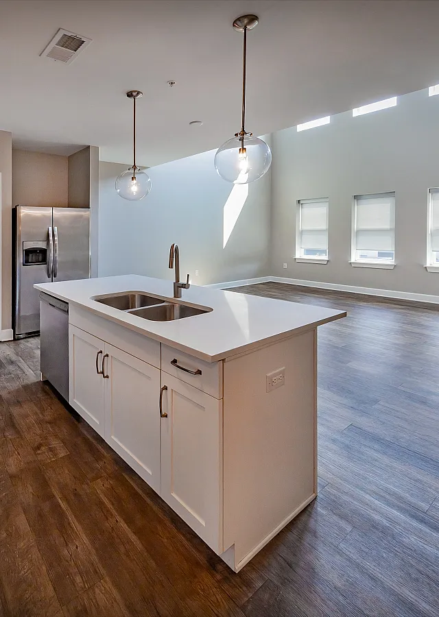 Modern kitchen with elegant pendant lighting, sleek island countertop, stainless steel appliances, and open living space with abundant natural light.