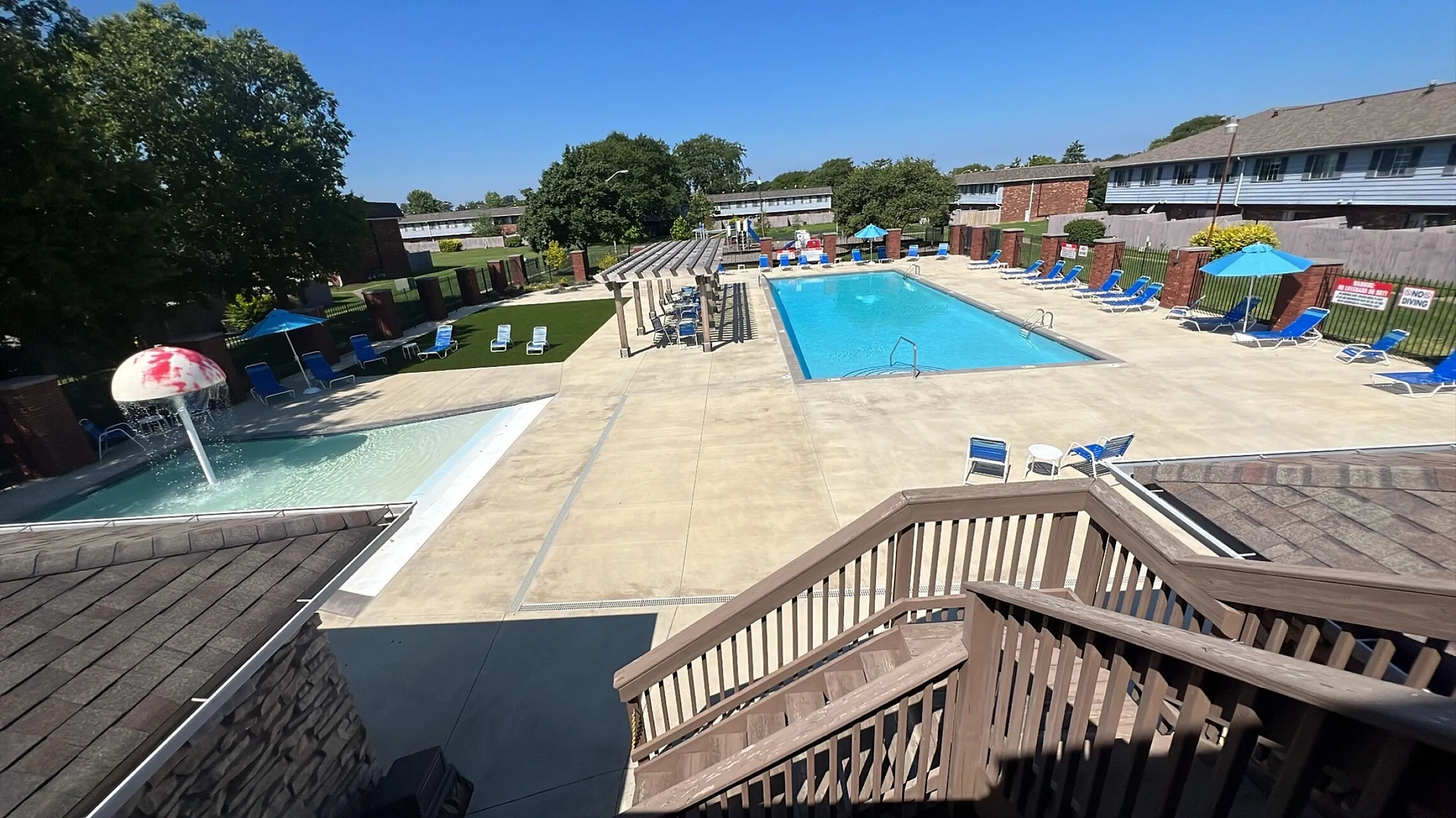Inviting outdoor pool area with sun loungers, perfect for relaxation, featuring a splash pad and sunny skies.