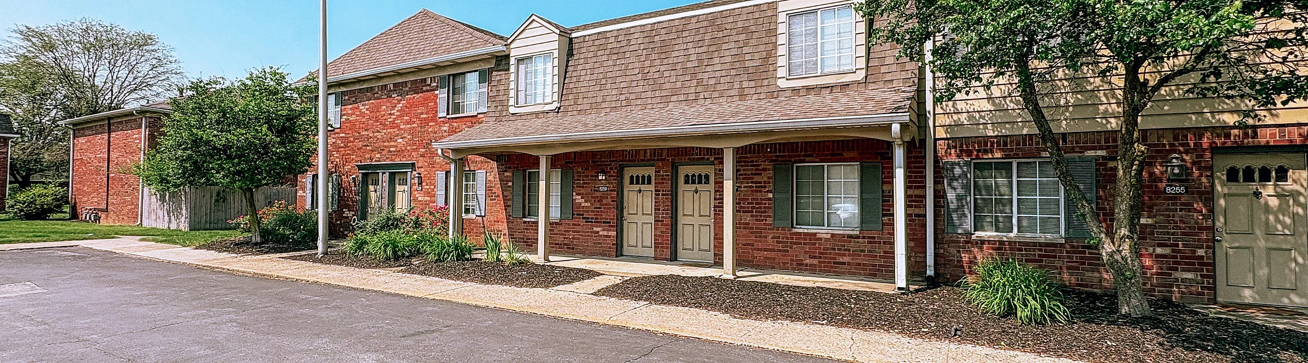 Inviting townhouse with charming brick facade and lush greenery, ideal for serene suburban living.