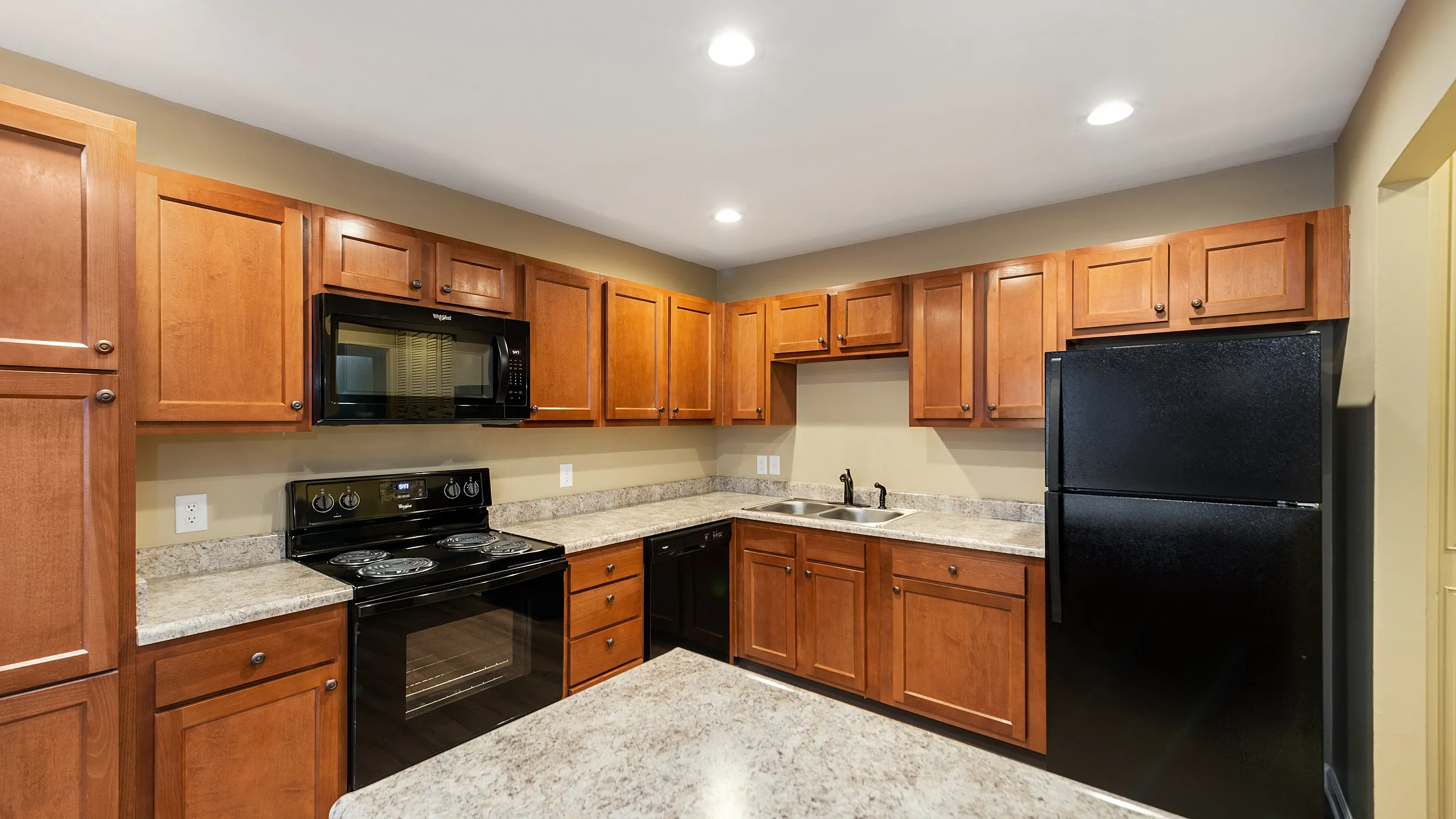 Modern kitchen with elegant wooden cabinets, sleek black appliances, and spacious granite countertops.