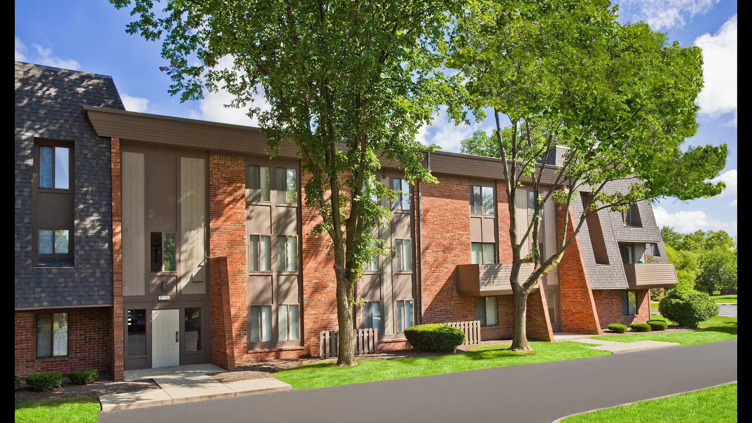Charming brick apartment complex surrounded by lush green trees, offering a cozy and inviting atmosphere.