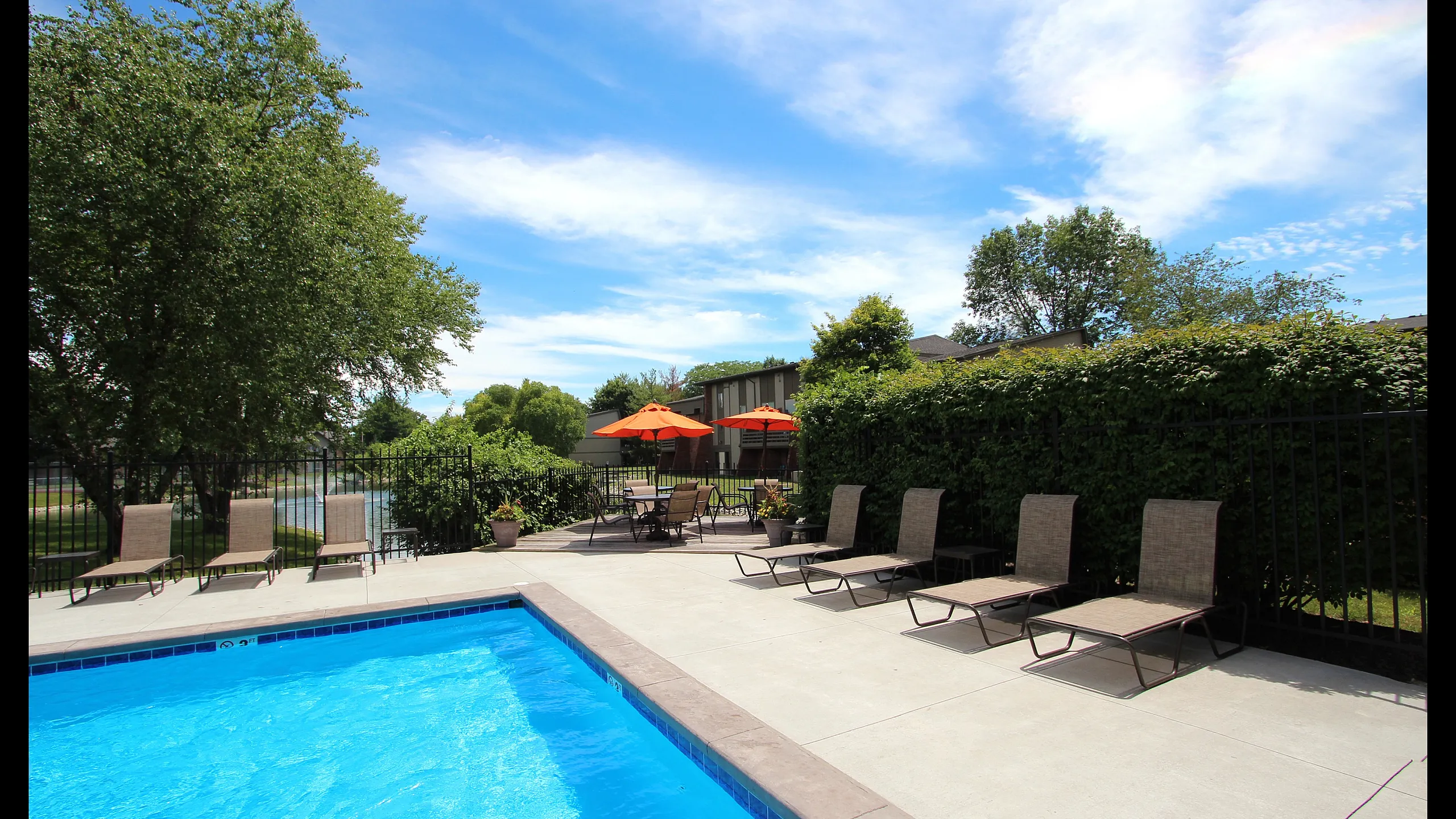 Inviting outdoor pool area with comfortable lounge chairs and vibrant orange umbrellas, perfect for relaxation and socializing.