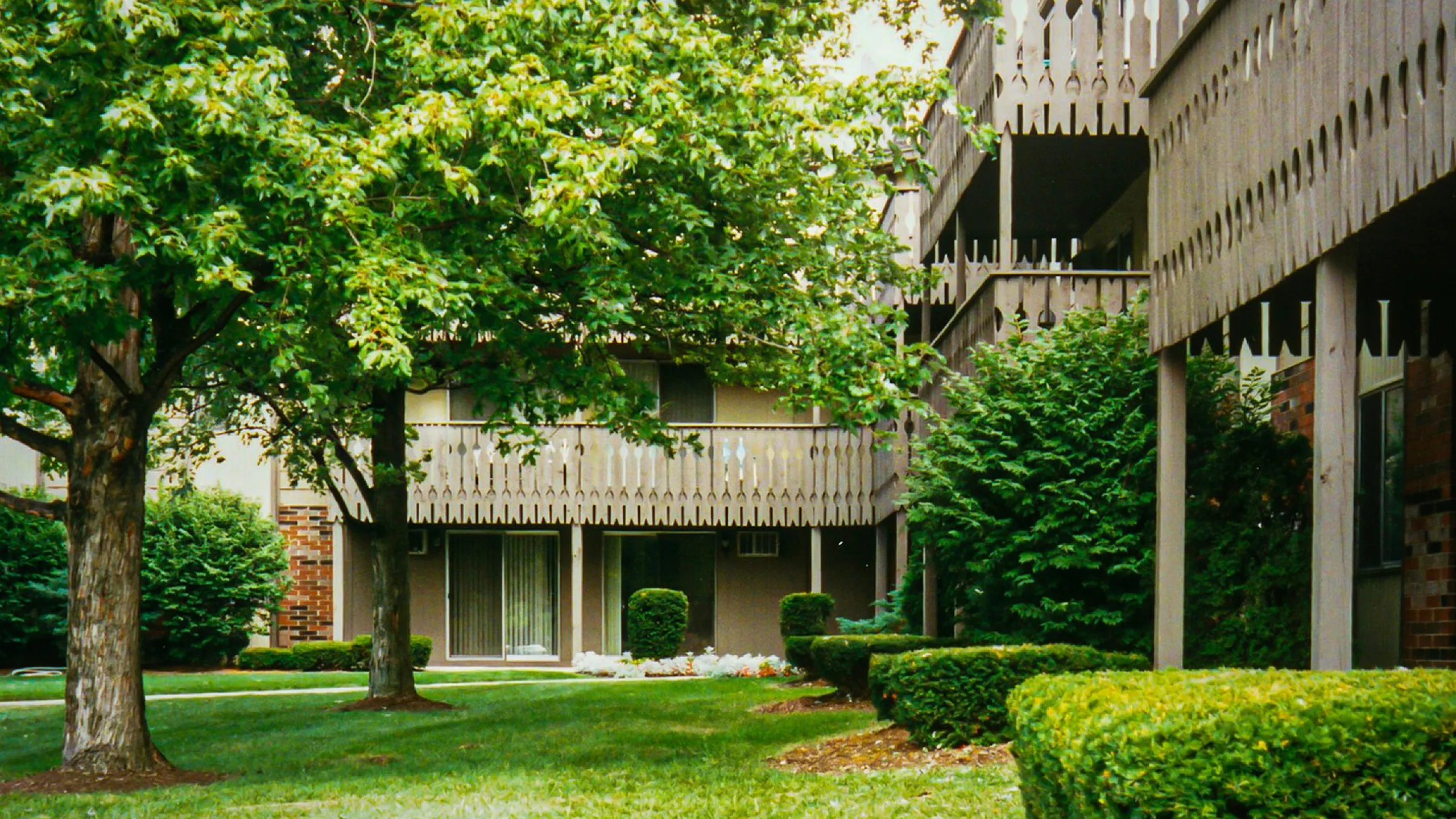 Charming apartment complex with lush greenery, decorative wooden balconies, and serene garden views.