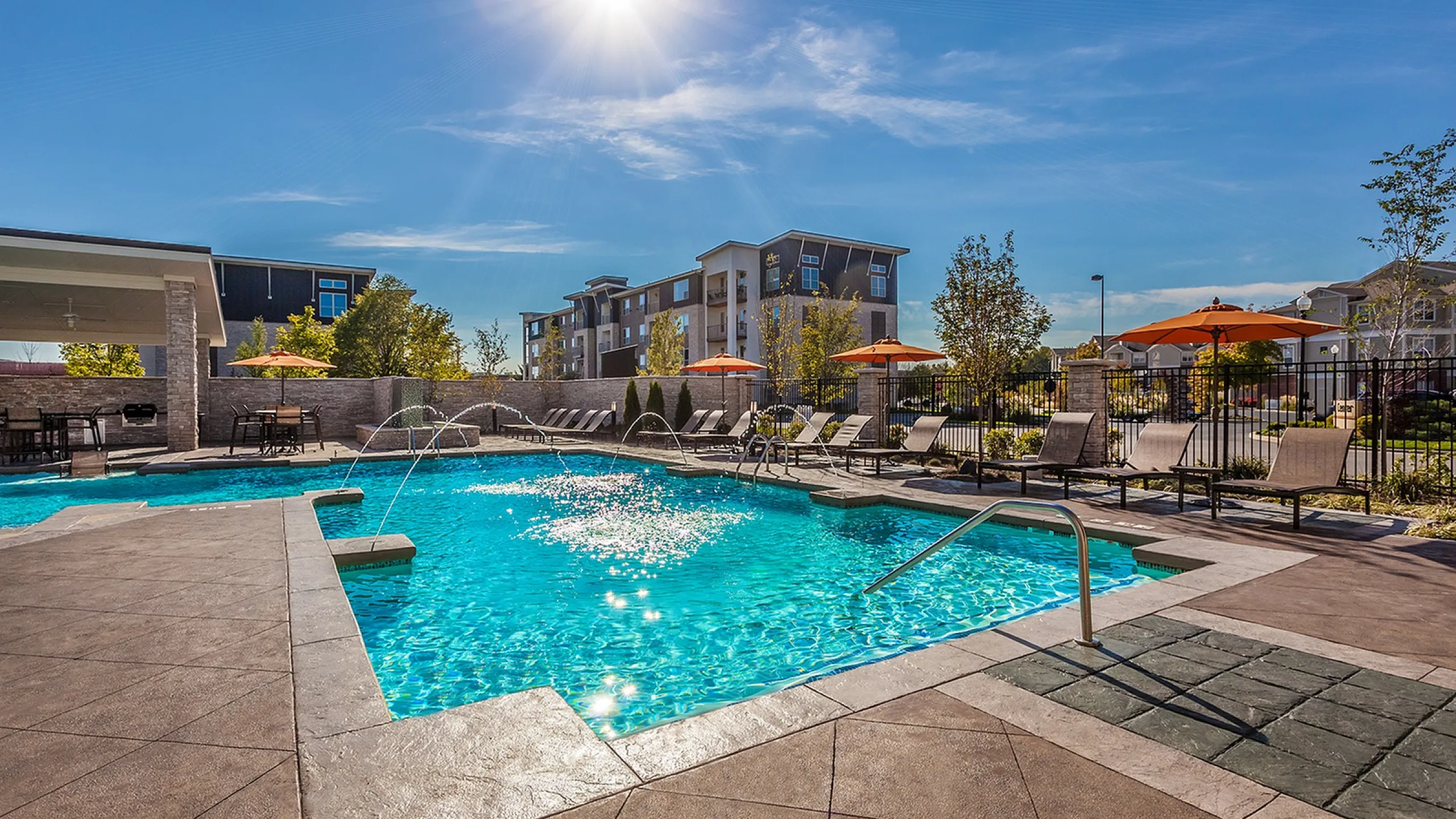 Luxurious apartment pool area with sparkling water, sun loungers, and umbrellas, perfect for relaxation and enjoyment under a bright blue sky.