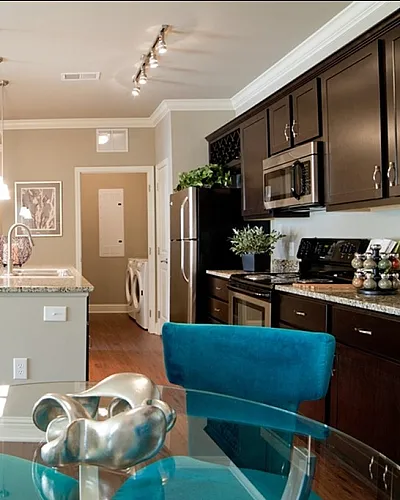 Chic apartment interior showcasing modern kitchen with dark cabinets, stylish pendant lighting over a breakfast bar, and vibrant turquoise chairs, creating a warm and inviting dining space.