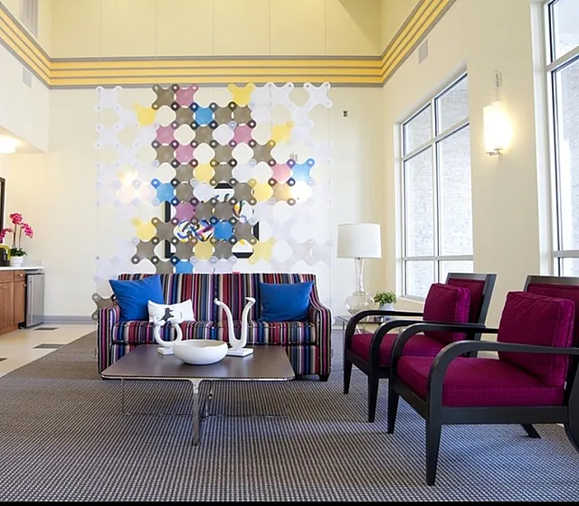 Chic and welcoming apartment lobby featuring vibrant decor, plush seating, modern art, and large windows for ample natural light.