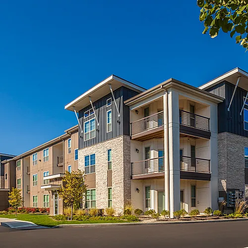 Modern three-story apartment building with sleek balconies and contemporary design under a clear blue sky.