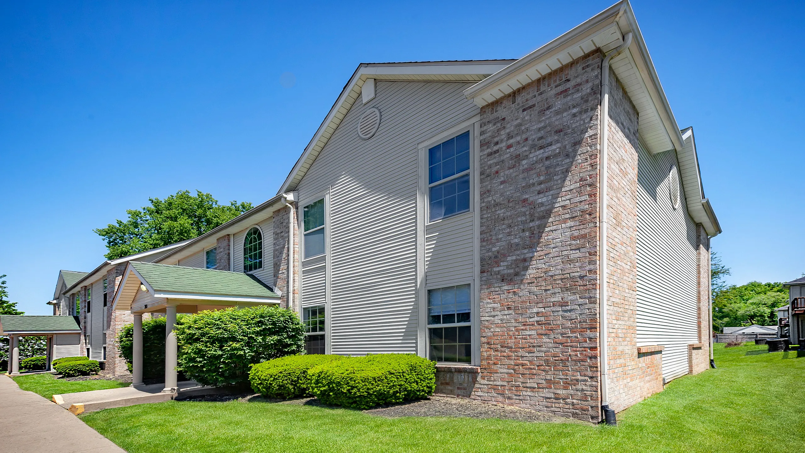 Charming residential apartment exterior with classic brick design and lush green landscaping under a clear blue sky.
