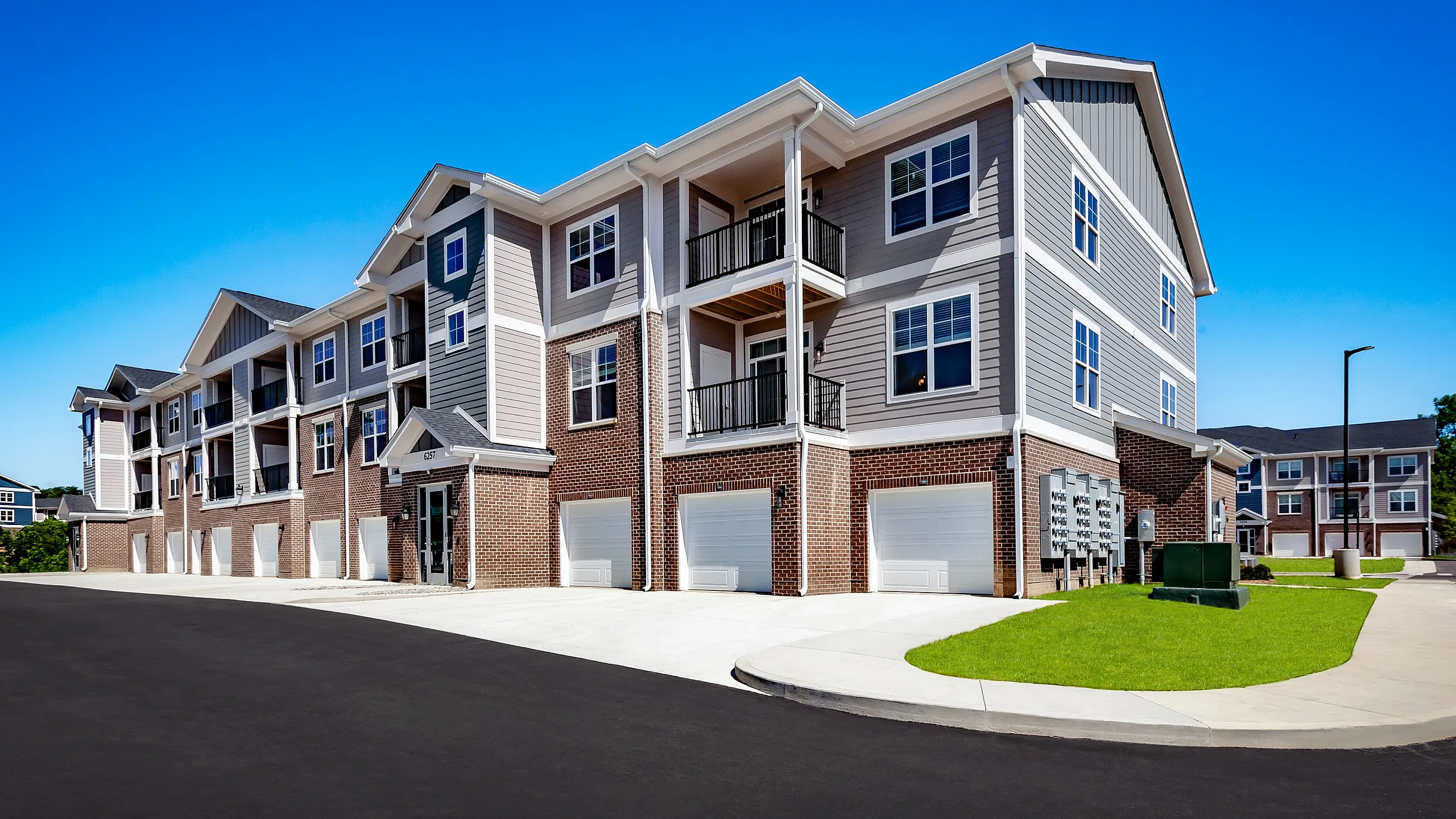 Modern apartment building with stylish brick and siding facade, featuring spacious balconies and attached garages on a sunny day.