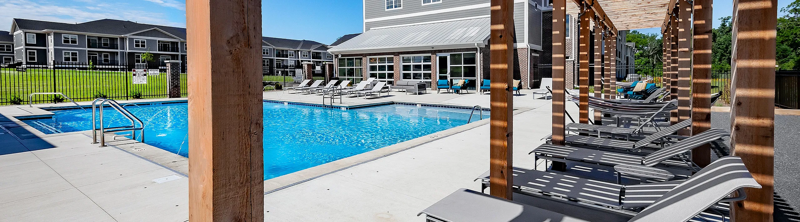 Luxurious poolside retreat featuring sun loungers under stylish pergolas, with a sparkling blue pool and modern clubhouse in the background.