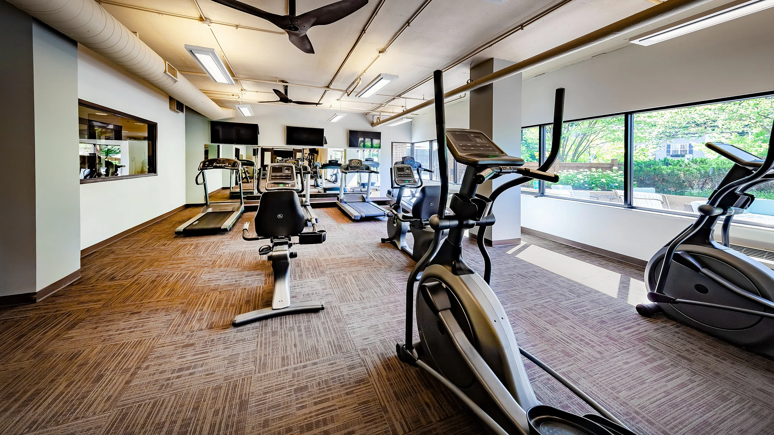 Bright and modern fitness center featuring state-of-the-art cardio equipment and large windows with a garden view.