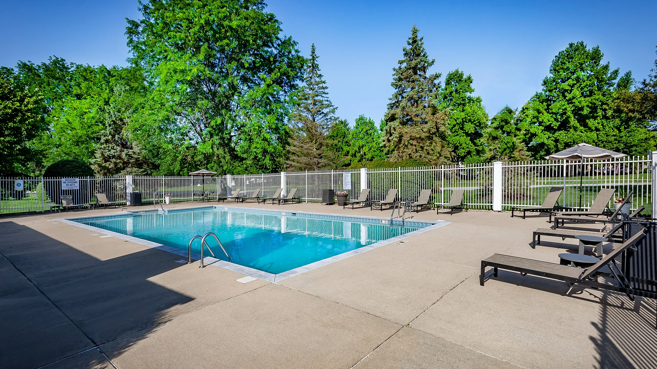 Inviting outdoor pool area surrounded by lush greenery and comfortable lounge chairs, perfect for relaxation and summer fun.