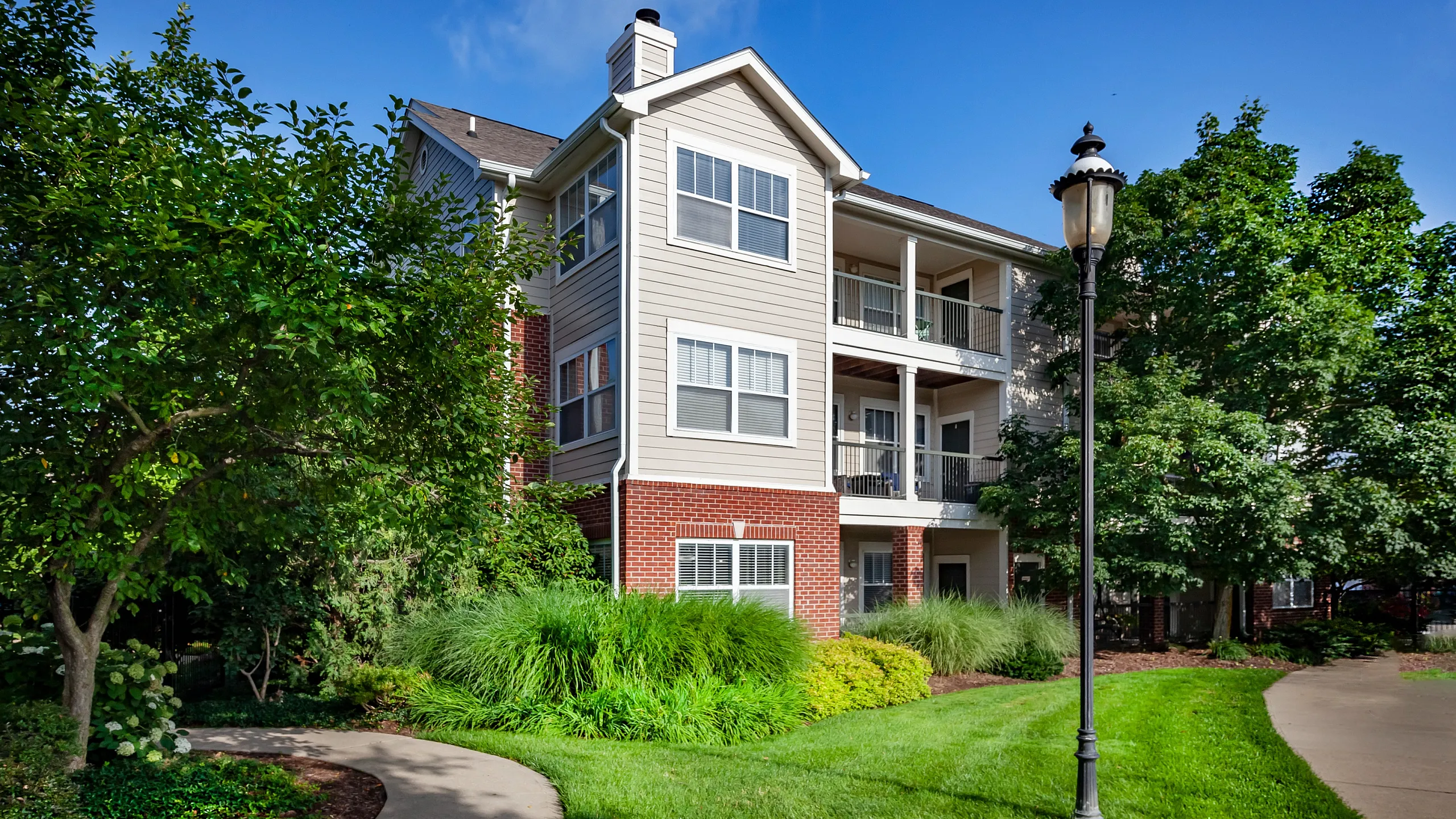 Charming apartment building with elegant balconies, nestled among lush greenery and manicured lawns.