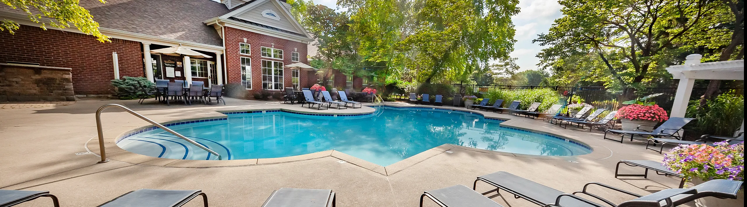 Inviting outdoor pool area with sun loungers, vibrant flowers, and a charming clubhouse surrounded by lush greenery.