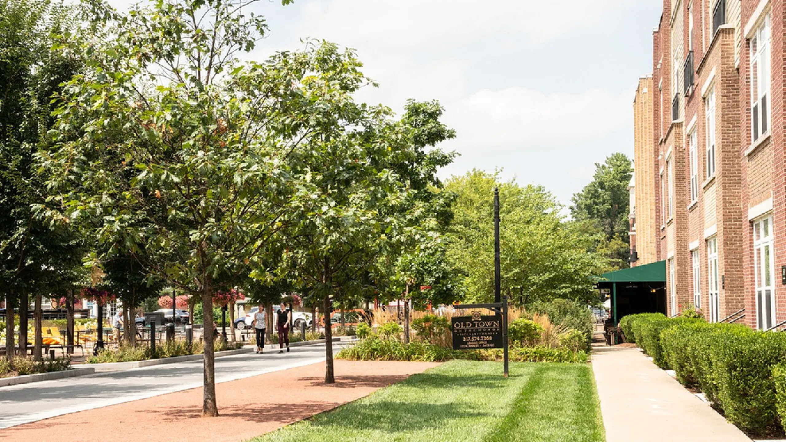 Old Town on the Monon Charming urban scene with lush greenery lining a walkway next to elegant brick apartment buildings, creating a peaceful and inviting atmosphere.