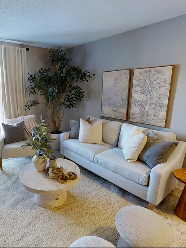 Pebble Point modern living room with elegant decor, featuring a cozy sofa, stylish armchair, and chic coffee table. Large windows with vertical blinds allow natural light to fill the space, while tasteful artwork and indoor plants add charm