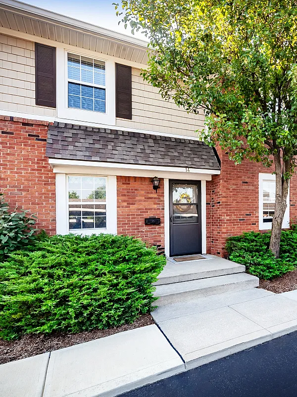 Charming brick townhouse with lush green landscaping and a welcoming front porch, ideal for serene living.