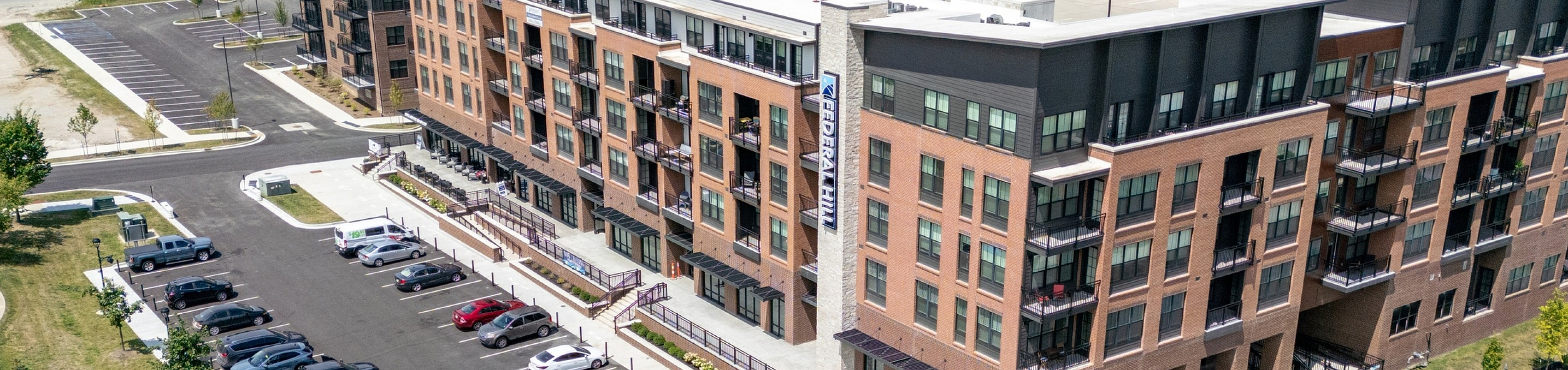 Aerial view of a modern apartment complex with elegant architecture, surrounded by lush greenery, ample parking, and a vibrant playground, offering a perfect blend of style and community convenience.