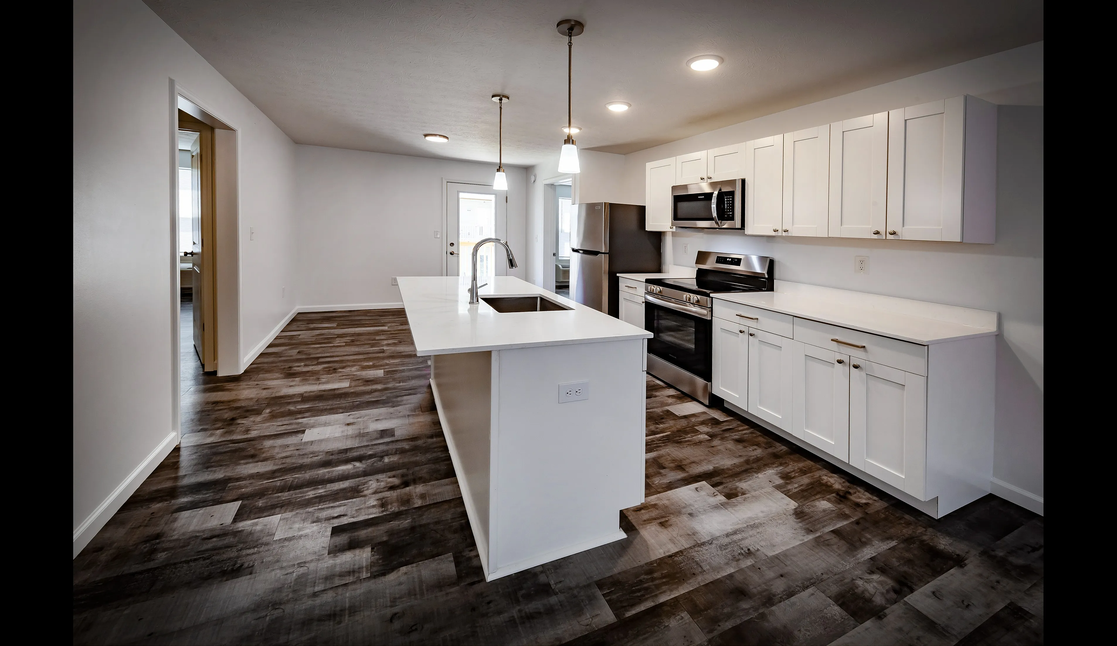 Reserve at Madison Flatts-Modern kitchen with sleek white cabinetry, stainless steel appliances, and elegant wood floors, featuring a stylish island with pendant lighting.