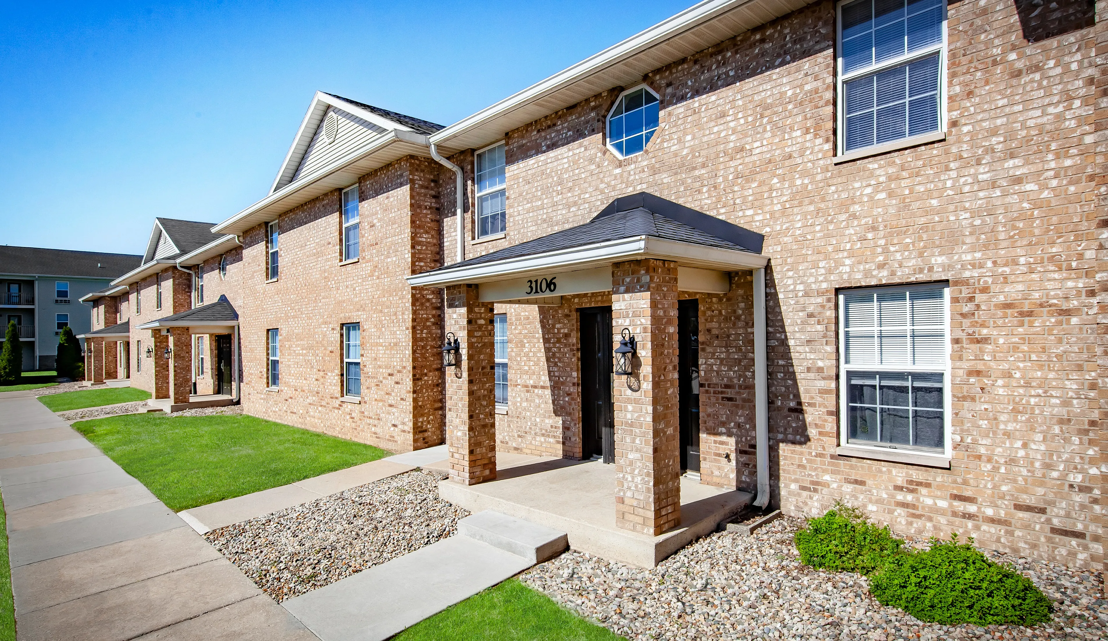 Reserve at Madison Flatts Charming brick apartment building with manicured green lawns and inviting entryways, showcasing a serene and welcoming community.