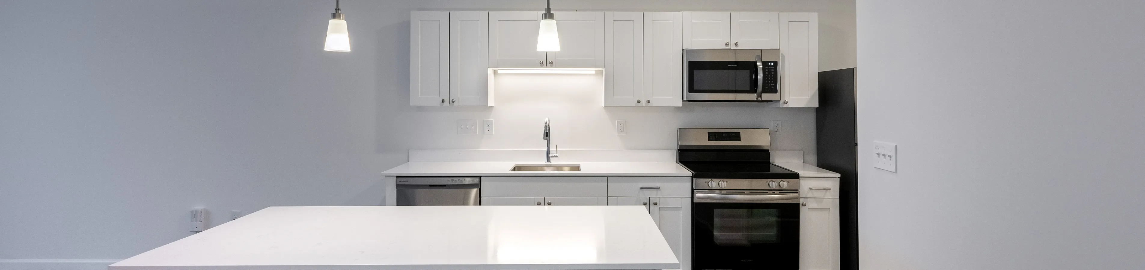 Reserve at Madison Flatts Modern kitchen with sleek white cabinetry, a spacious island, and stainless steel appliances, perfect for culinary adventures.