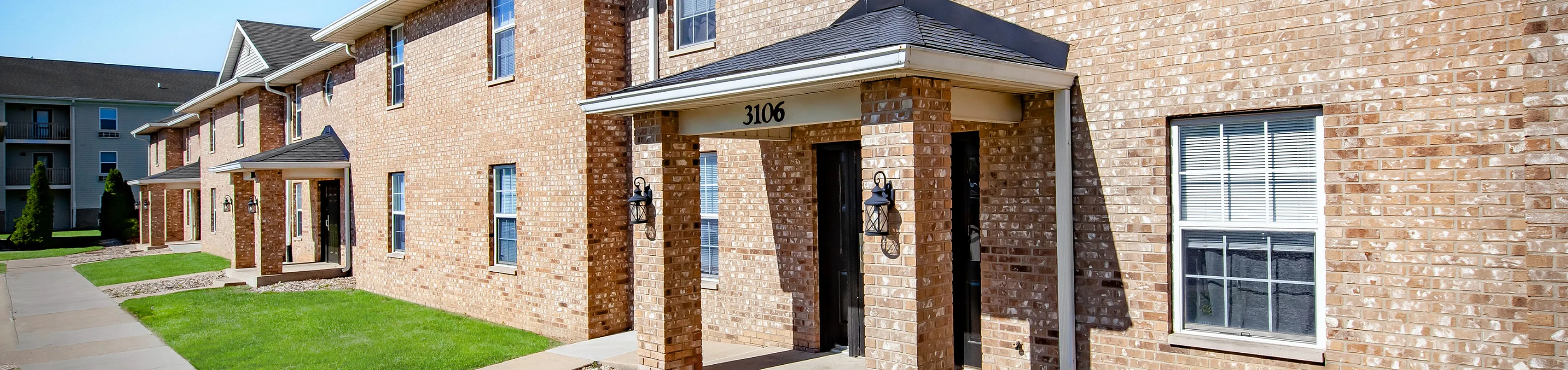Reserve at Madison Flatts charming brick apartment exterior with lush green lawns and inviting entrance, perfect for modern living.
