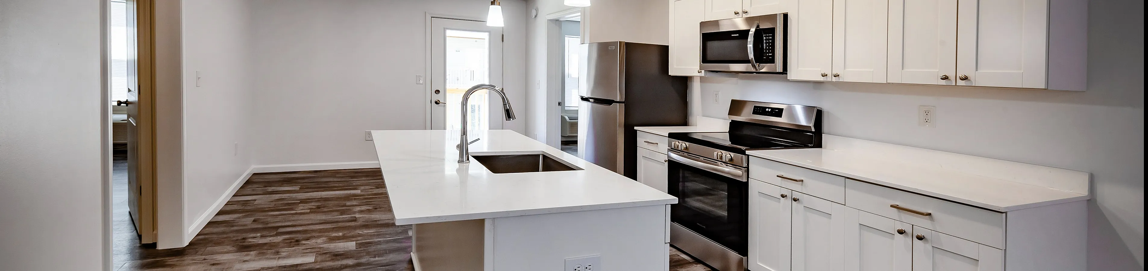 Sleek modern kitchen with stainless steel appliances, stylish pendant lighting, and a spacious island in a bright open layout.