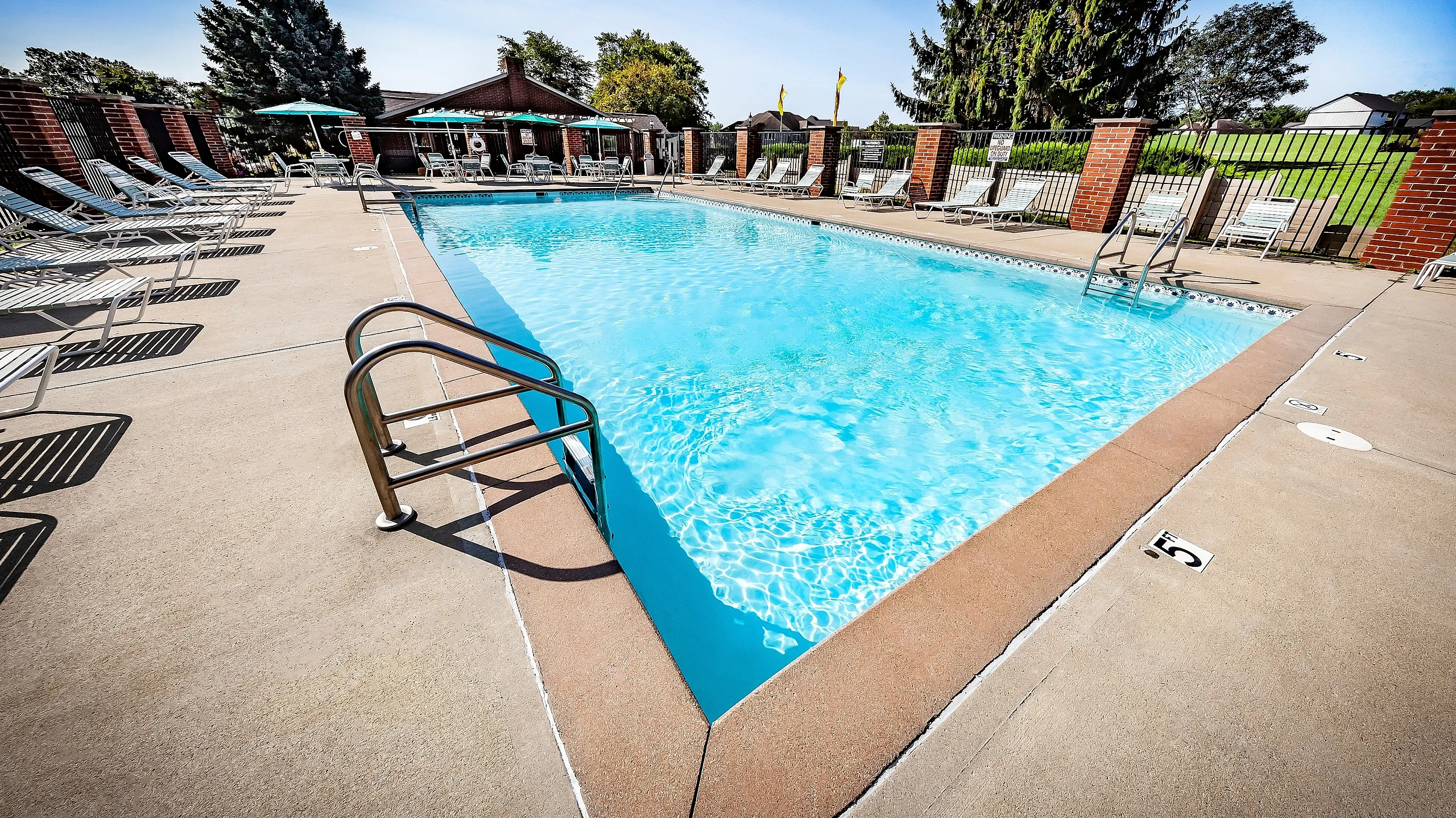 Greenfield Crossing Apartments - Inviting outdoor pool area featuring crystal-clear water, elegant brick fencing, and plenty of sun loungers for relaxation.