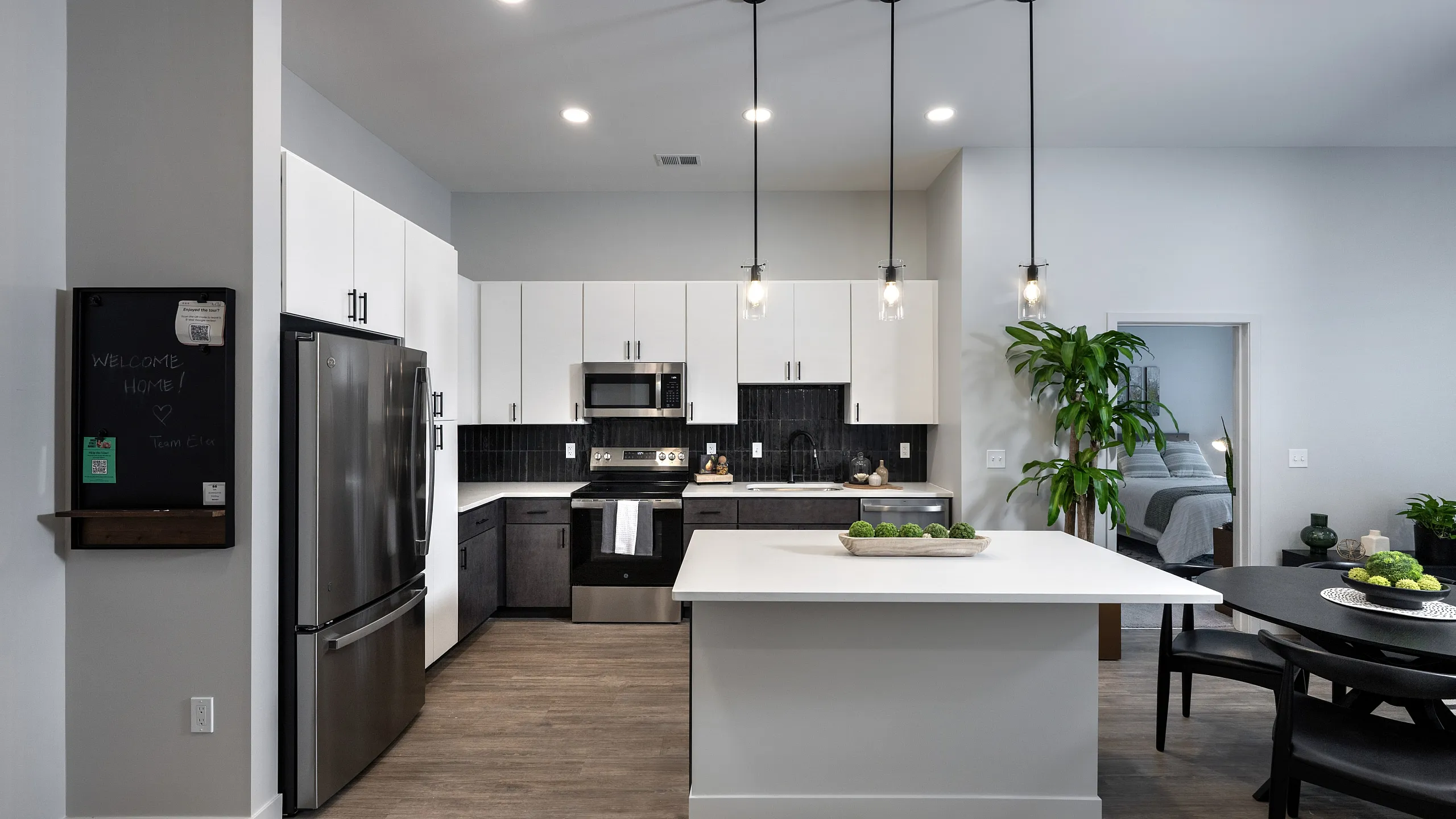 The Elex: Modern kitchen and dining area with sleek cabinetry, stainless steel appliances, and elegant pendant lighting, leading to a cozy bedroom.