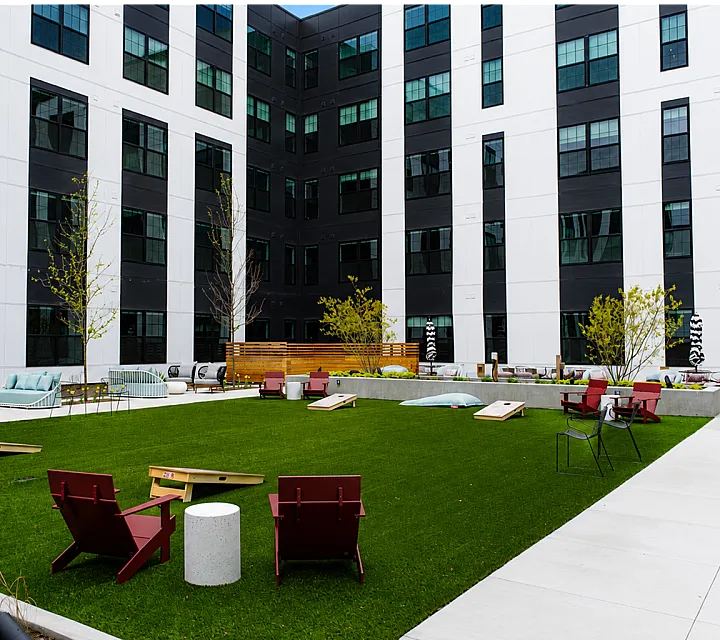 The Elex: Modern urban courtyard featuring lush green lawn, stylish patio furniture, and recreational space in a contemporary apartment complex.
