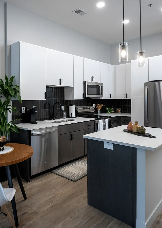 The Elex: Modern kitchen with sleek white cabinetry, stainless steel appliances, and a cozy dining area with a stylish wooden table and white chairs.
