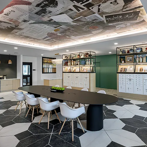 The Elex: Chic communal space with a modern black table, sleek white chairs, and decorative open shelving, featuring a striking patterned ceiling and floor.
