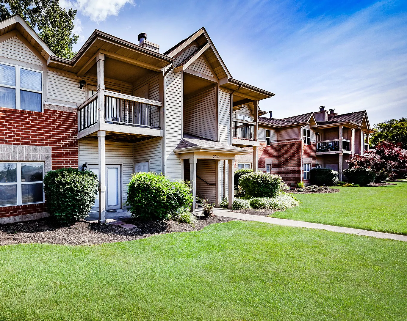 Charming apartment complex showcasing modern design with lush greenery, brickwork, and spacious balconies, perfect for serene living.