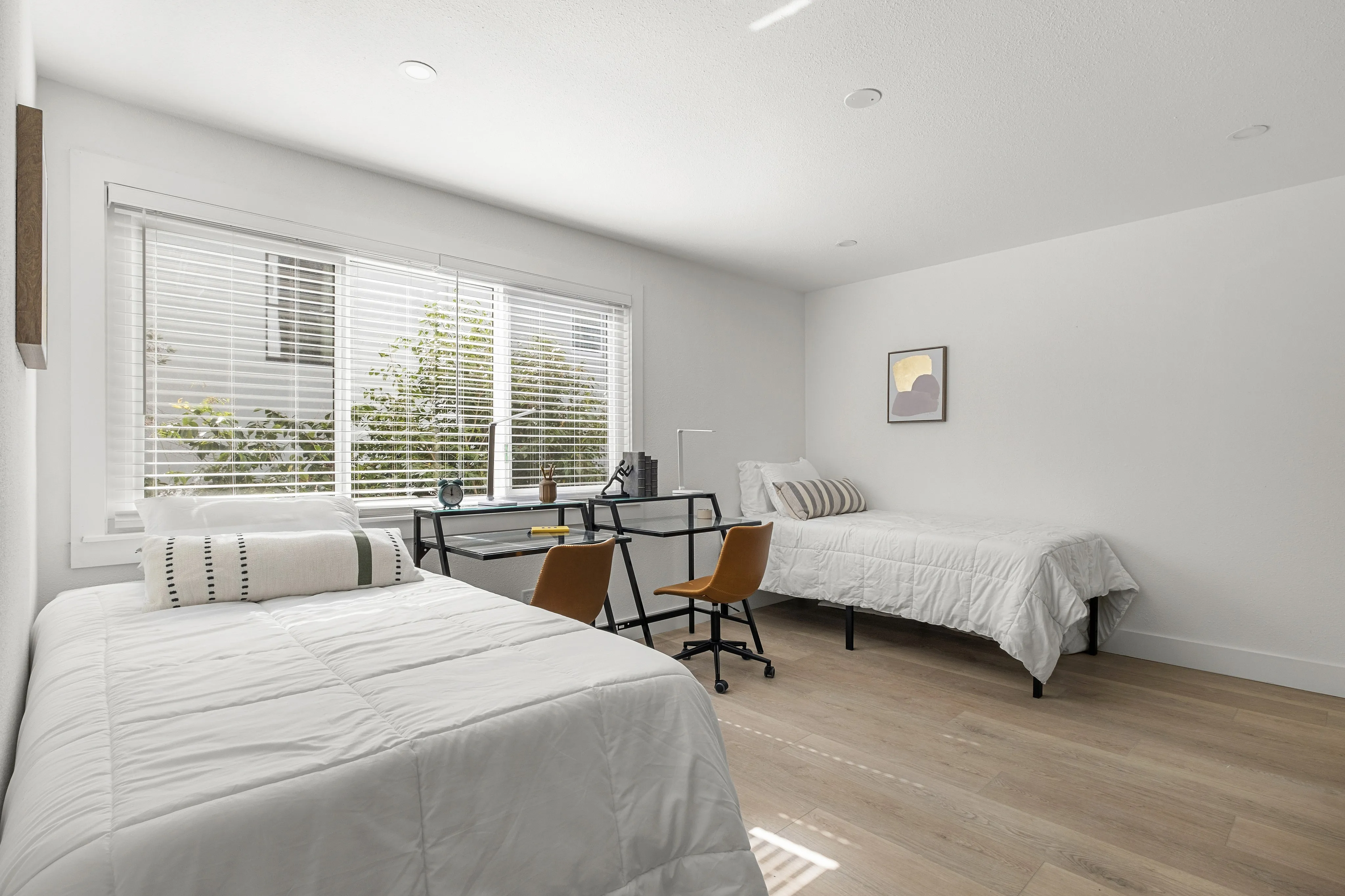 Bright and inviting bedroom with two cozy beds, a modern study desk, and large windows allowing natural light.