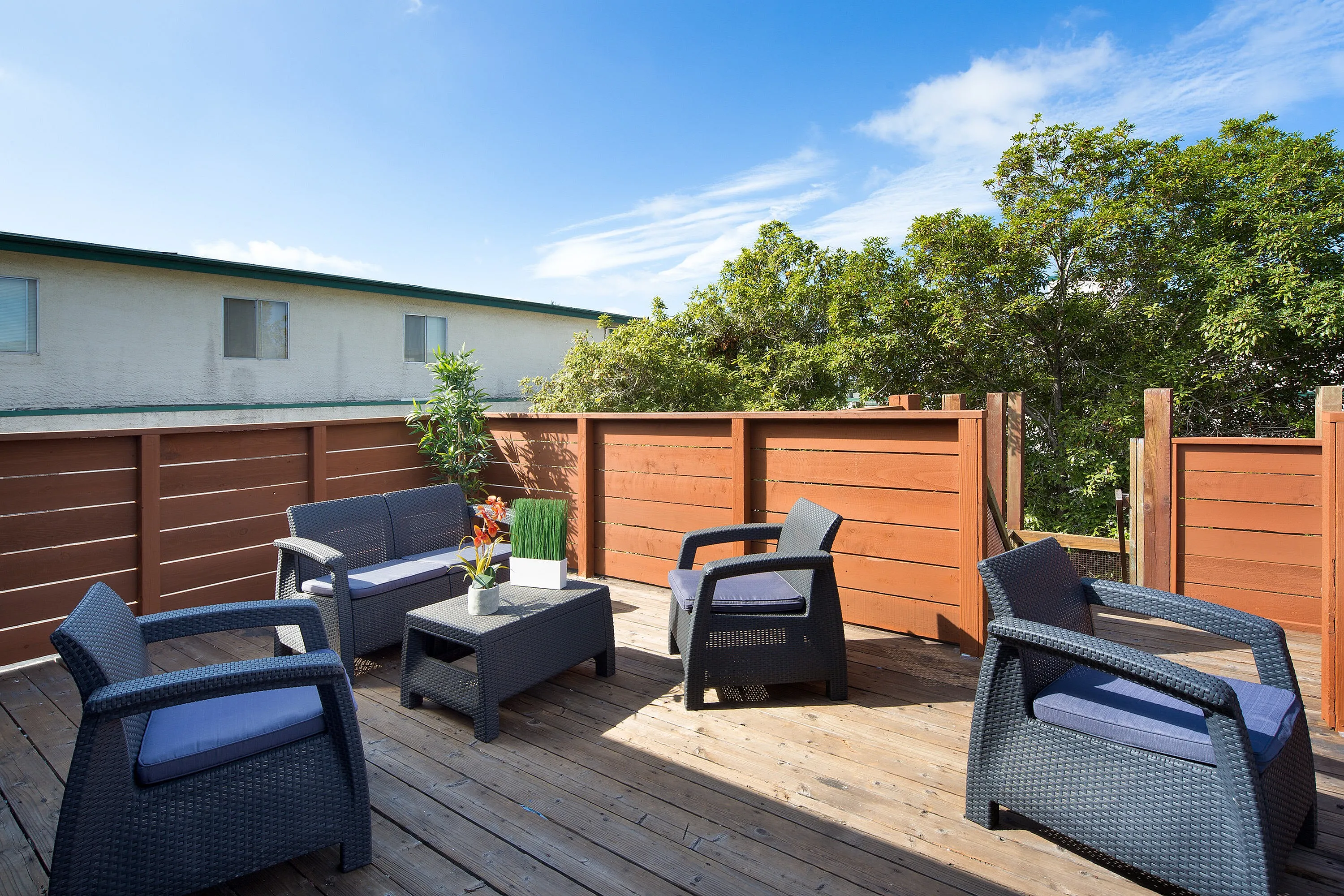 Inviting rooftop terrace with stylish wicker seating, surrounded by lush greenery and bathed in sunshine.