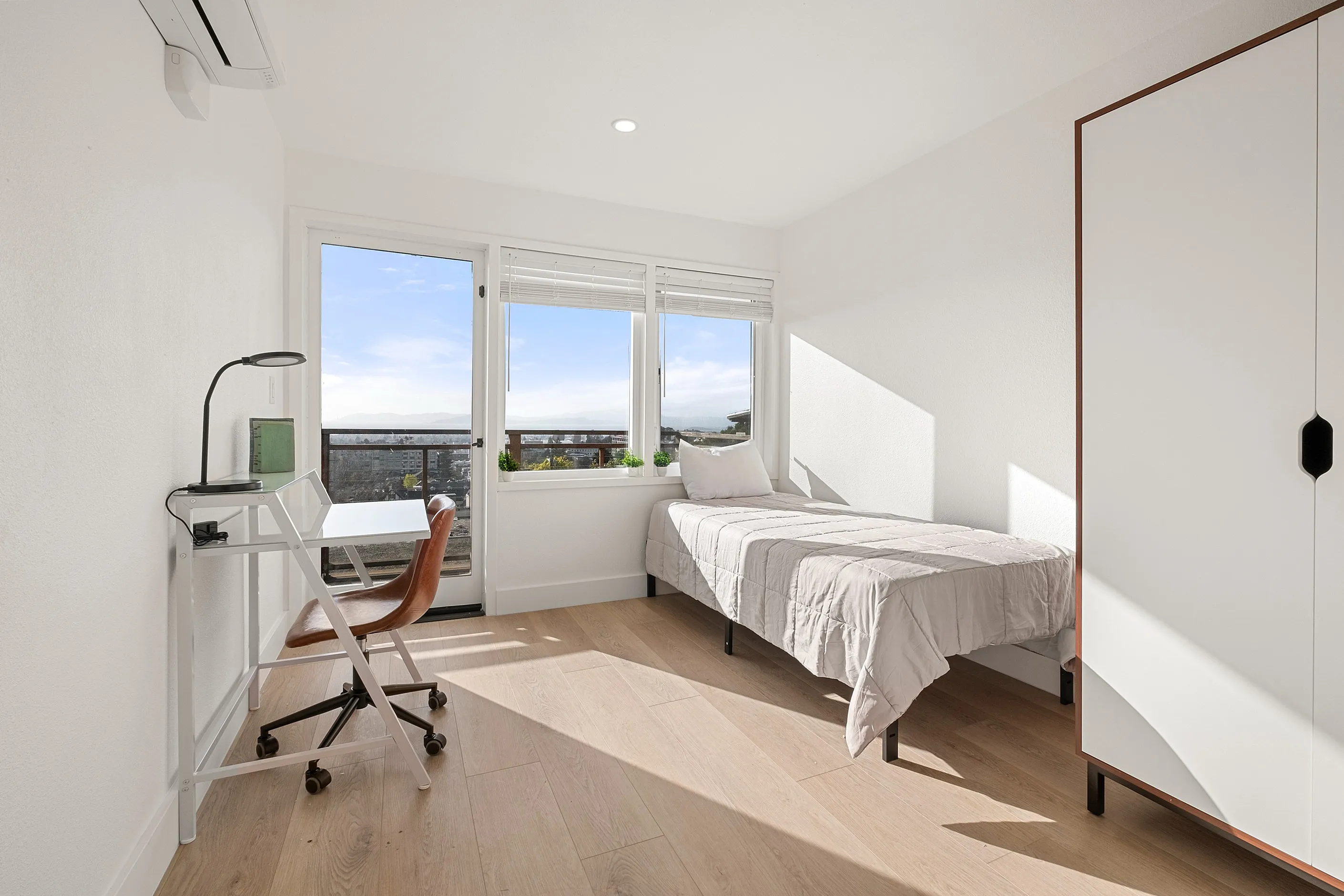 Bright and airy bedroom featuring a comfortable single bed, study desk, and large window offering stunning city views.